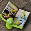 Kermit the frog sits on the paved road and reads a book about Kermit the frog
